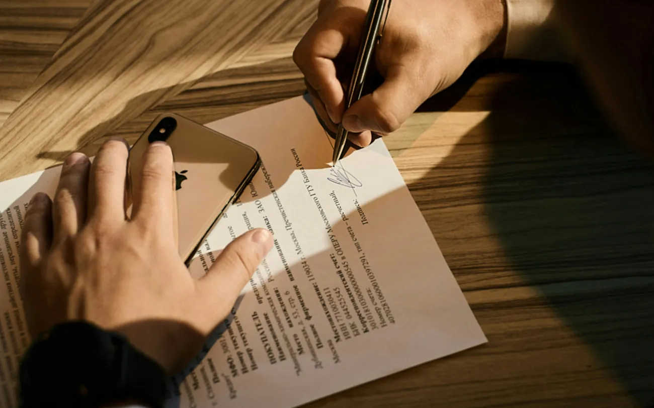 A contract being signed on a wooden desk